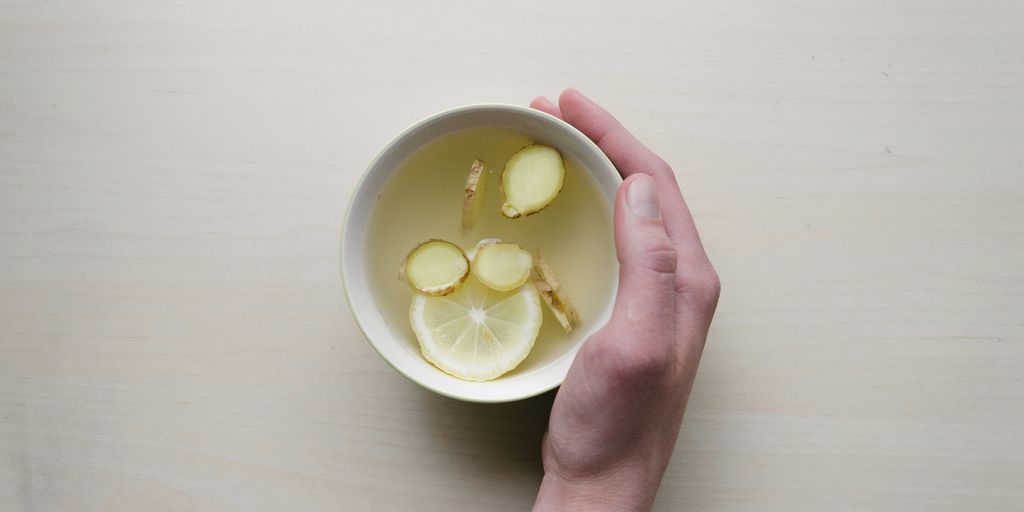 person holding white bowl with sliced lime and ginger inside