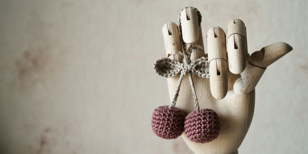 a wooden hand with two knitted balls hanging from it