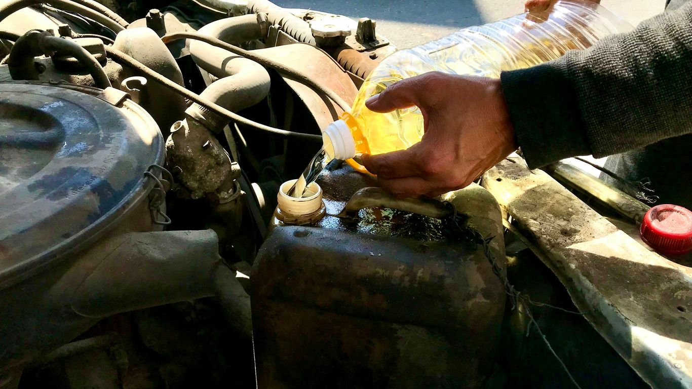 a man is filling a bottle of liquid into a car's engine