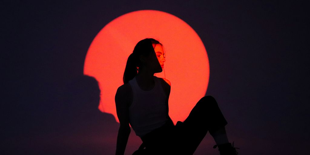 a silhouette of a woman sitting in front of a red sun