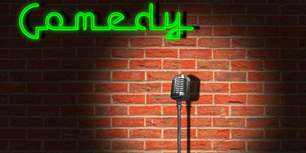 A microphone stands in front of a brick wall, "Comedy" sign.