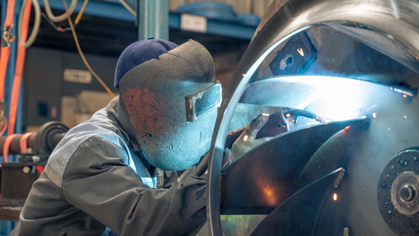 A worker welding a large metal turbine component in a workshop.