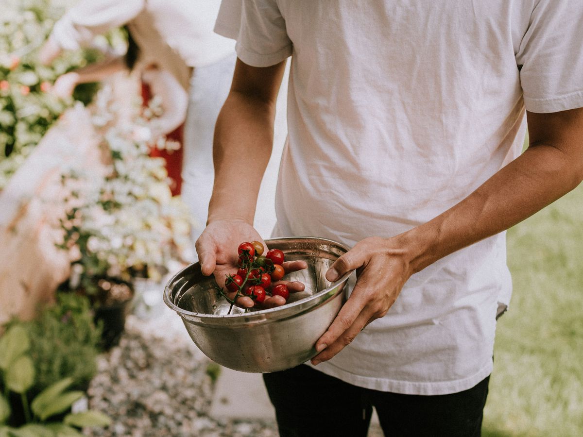 person in white t-shirt holding red round fruits