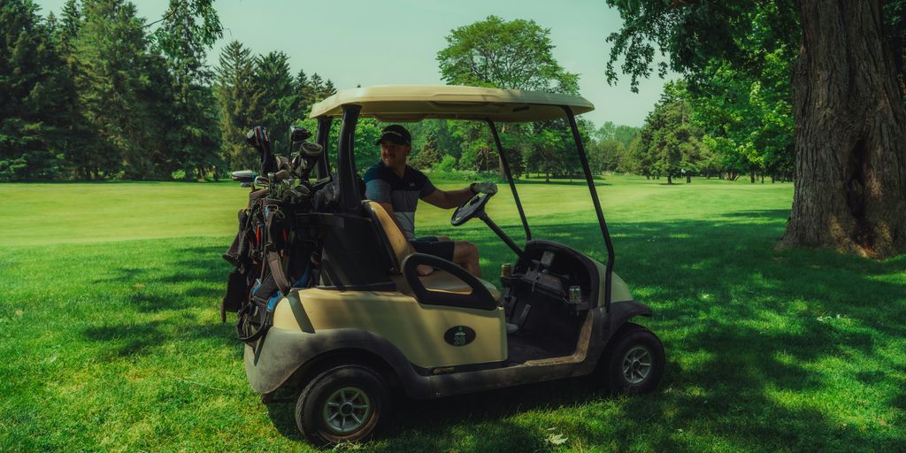Man drives a golf cart on a sunny golf course.