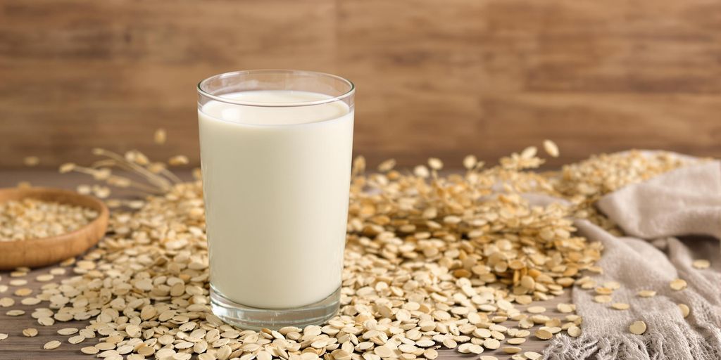 A glass of oat milk with oats scattered around.