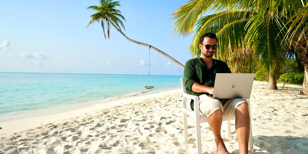 a man sitting in a chair on a beach using a laptop