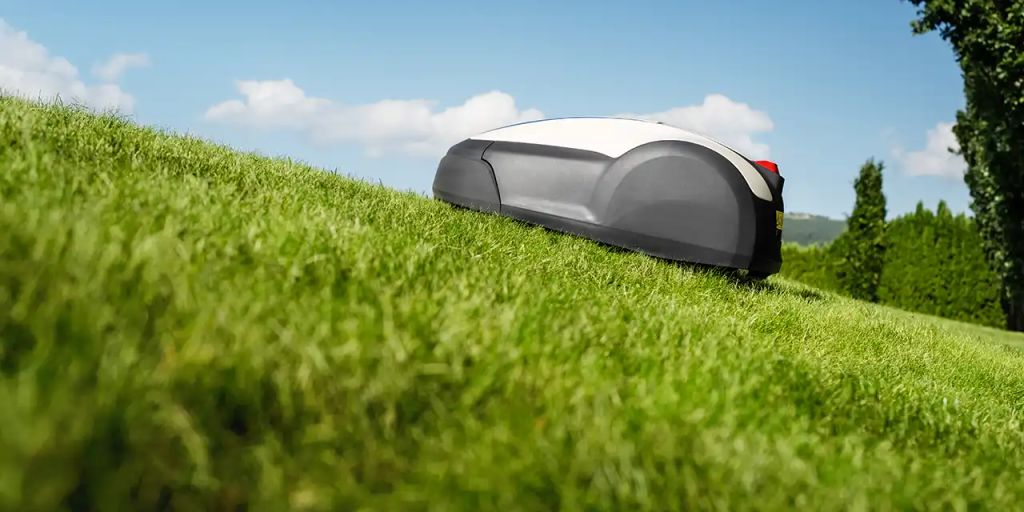 A robotic lawn mower on a grassy hill under clear skies.