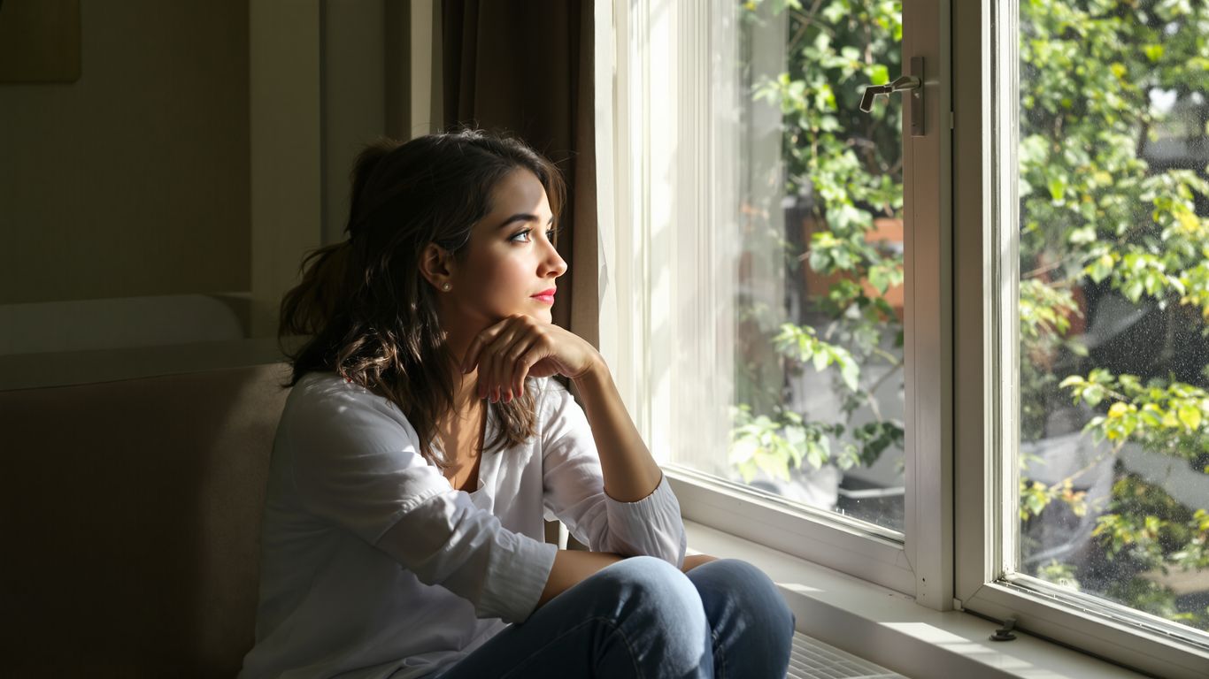 Young woman gazing thoughtfully out a sunlit window