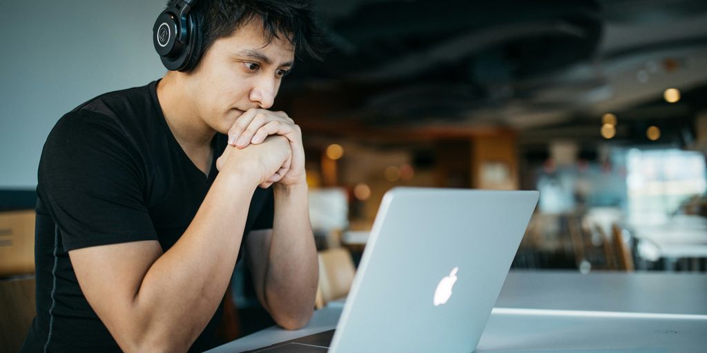 man wearing headphones while sitting on chair in front of MacBook