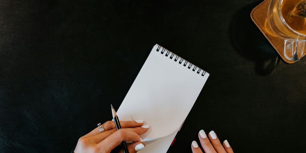 a woman writing on a notepad next to a cup of coffee