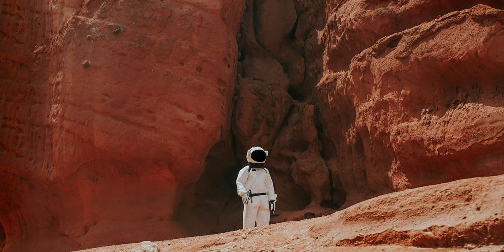 photography of astronaut standing beside rock formation during daytime