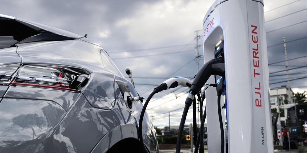 Electric vehicle charging at station under cloudy sky.