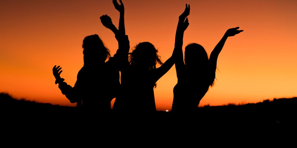silhouette of three woman with hands on the air while dancing during sunset