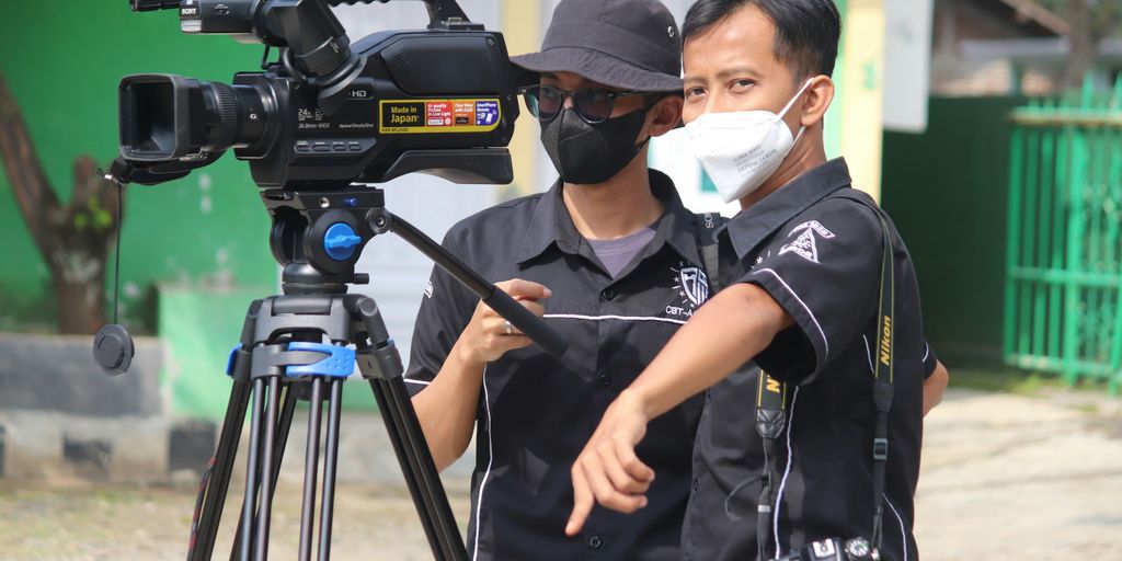 man in black polo shirt wearing white mask holding black camera