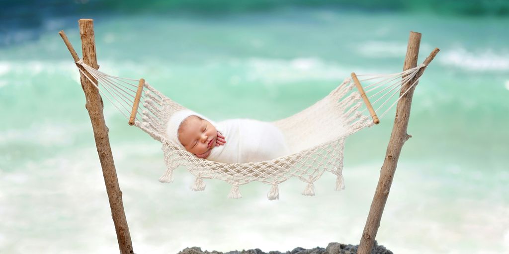 a baby laying in a hammock on the beach