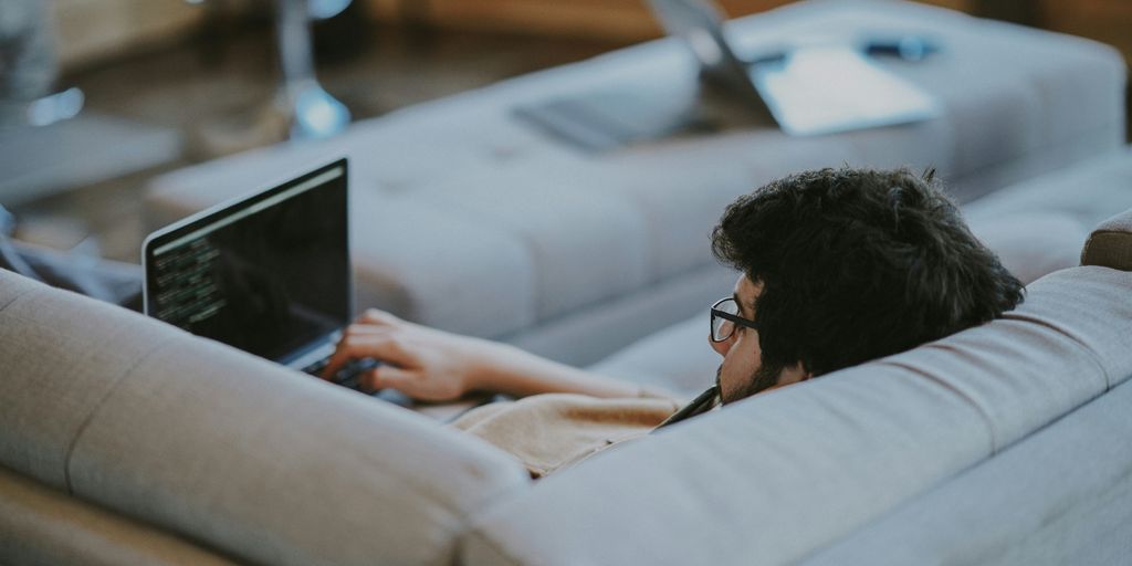 man lying on couch while using laptop computer