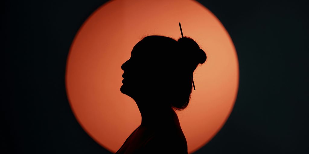 a silhouette of a woman in front of a sun