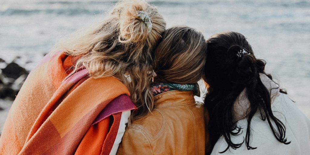 three women are sitting on a bench looking at the ocean