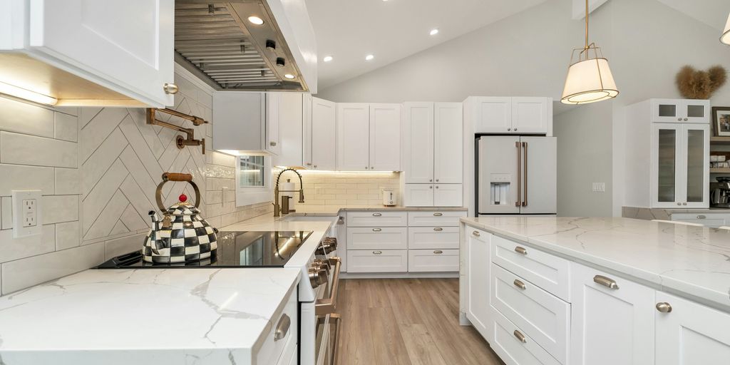 a kitchen with white cabinets and marble counter tops