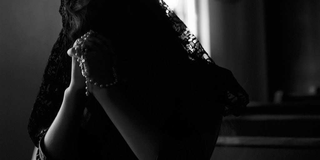 grayscale photography of woman praying while holding prayer beads