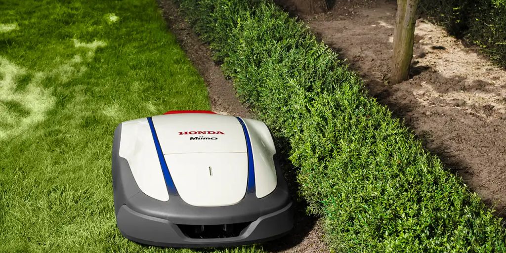 A robotic lawn mower trimming grass near hedges.
