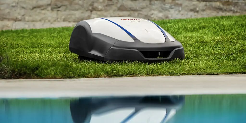 Robotic lawn mower on grass near a swimming pool.