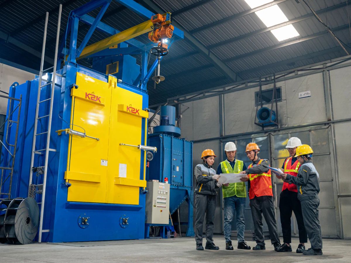 Group of workers discussing plans near industrial equipment indoors.