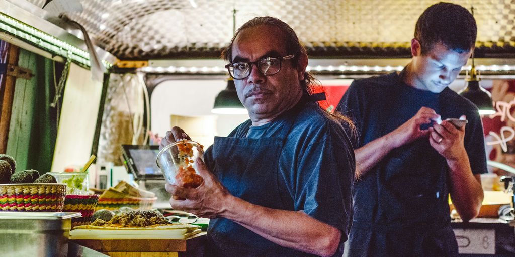 man holding clear glass beside man using cellphone at daytime