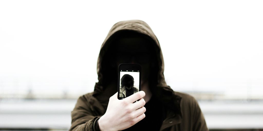 man wearing black hooded jacket and holding smartphone white taking close-up selfie