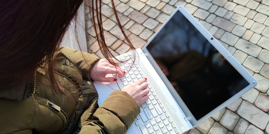 a woman is typing on her laptop outside