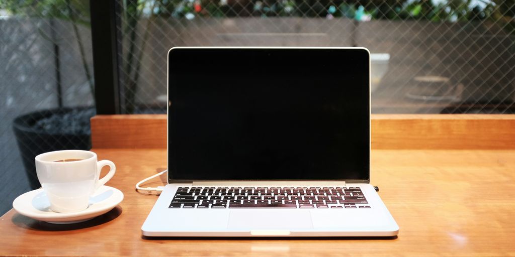 Laptop on a wooden table with a coffee cup, emphasizing preparation for virtual meetings and equipment checks.