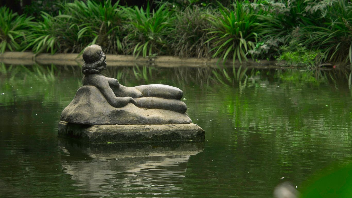 A statue of a person sitting on a rock in a pond