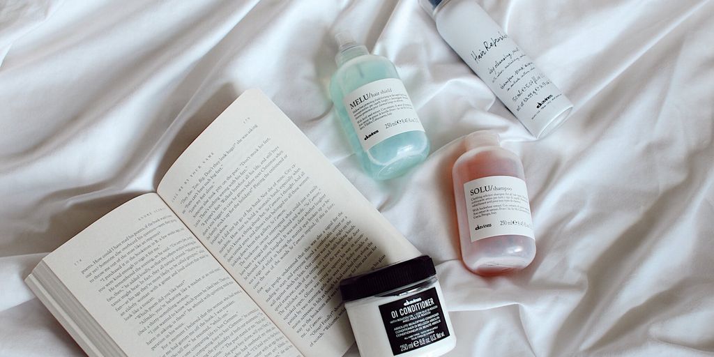 Skincare products and an open book on a white bedspread.