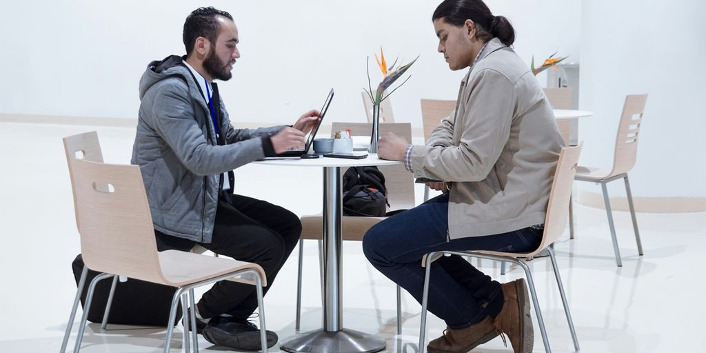 sitting man using laptop near woman sitting beside table