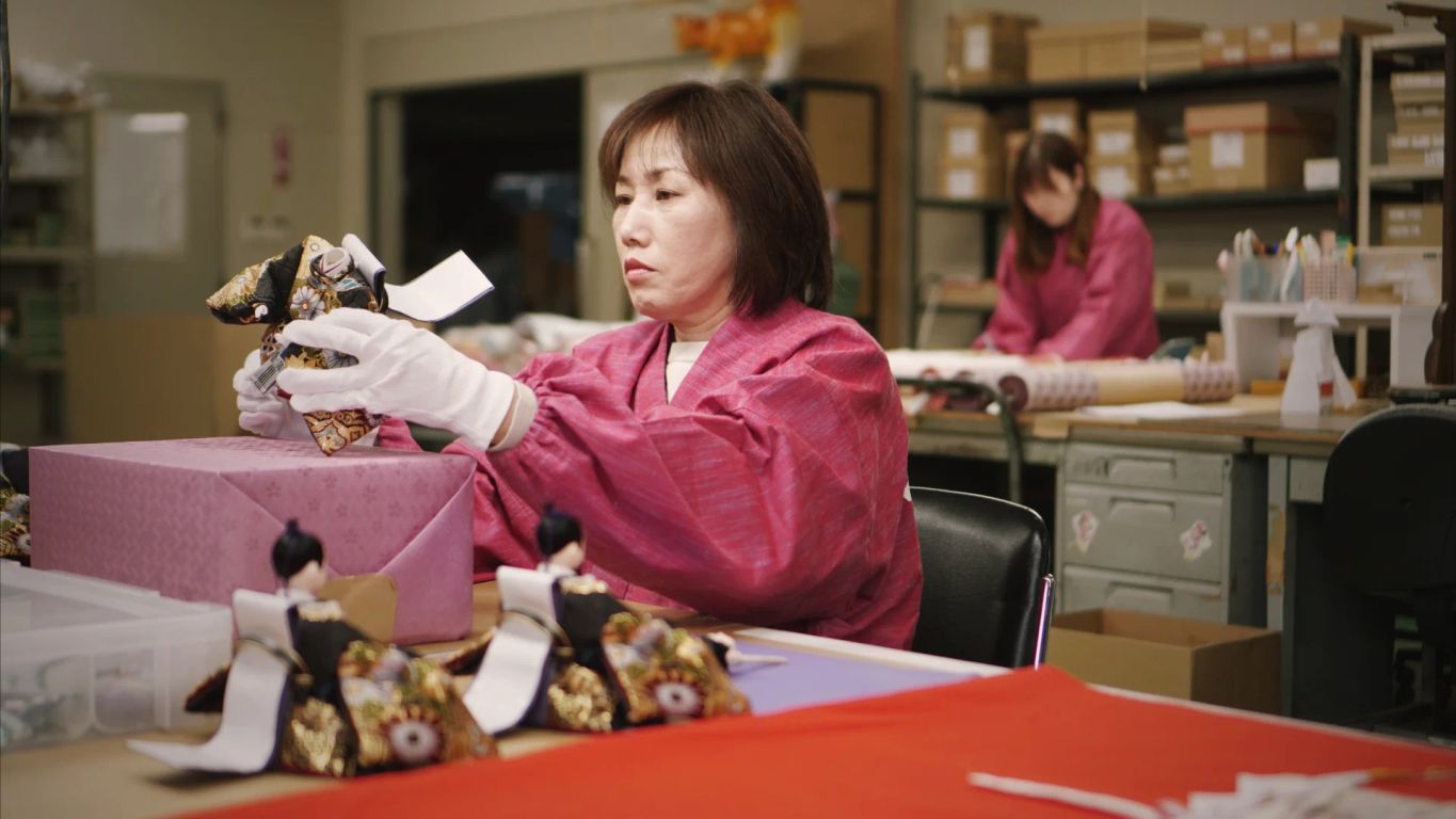 Two individuals wearing pink attire work on delicate handicrafts indoors.