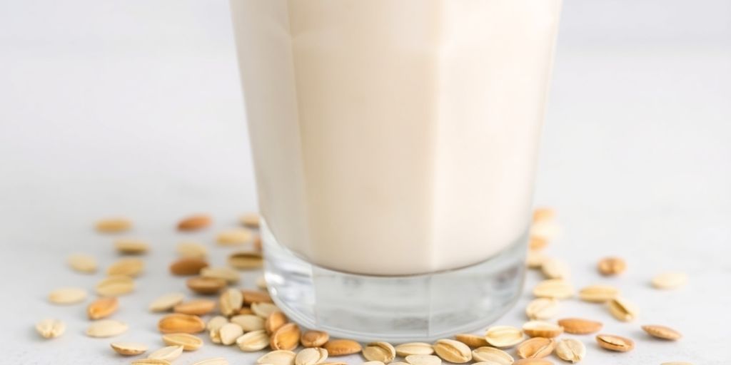 Creamy oat milk pouring into a glass with oats.