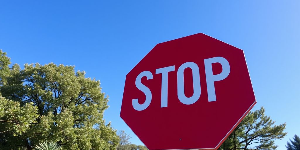 Red stop sign with blue sky and green trees.