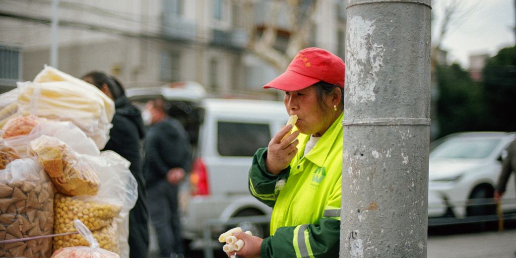 A street vendor enjoys a snack behind a post.
