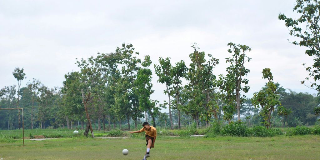 boy in brown shirt playing soccer on green grass field during daytime
