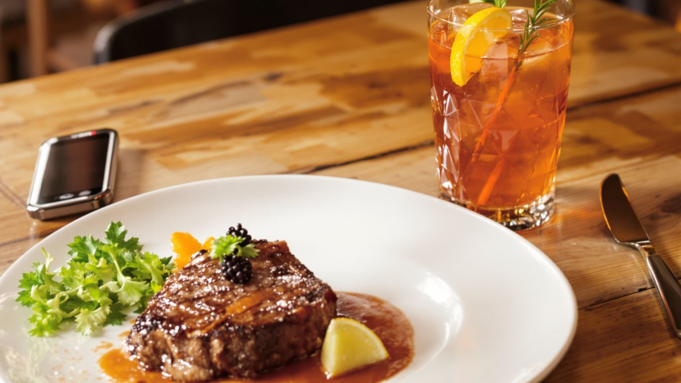 Juicy steak and colorful cocktail on a wooden table.