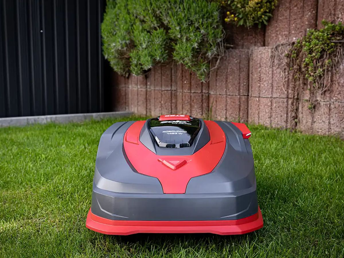 Robotic lawn mower on green grass near a wall.