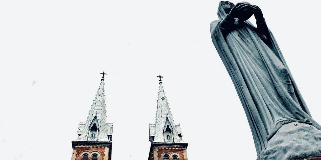 a statue of a person with their hand up in front of a church steeple