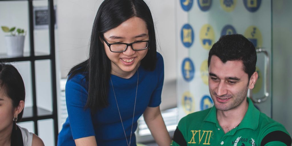 smiling woman standing beside smiling man pointing MacBook