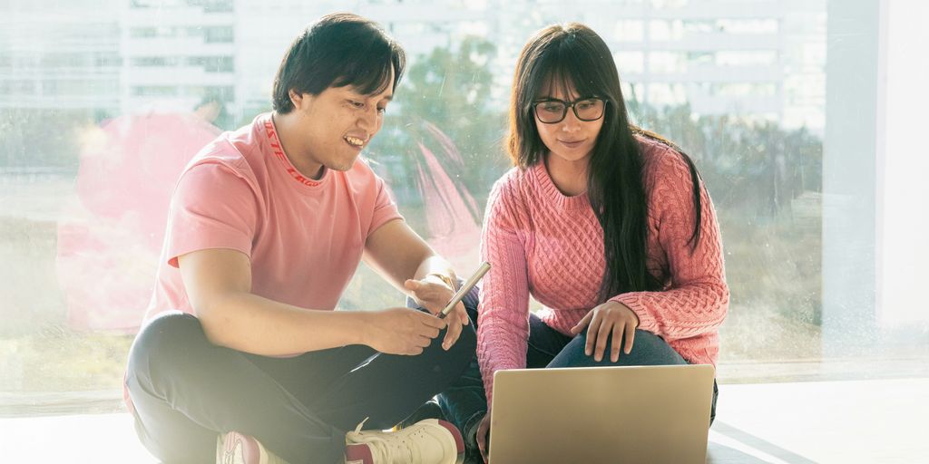 A man and a woman sitting on the floor with a laptop