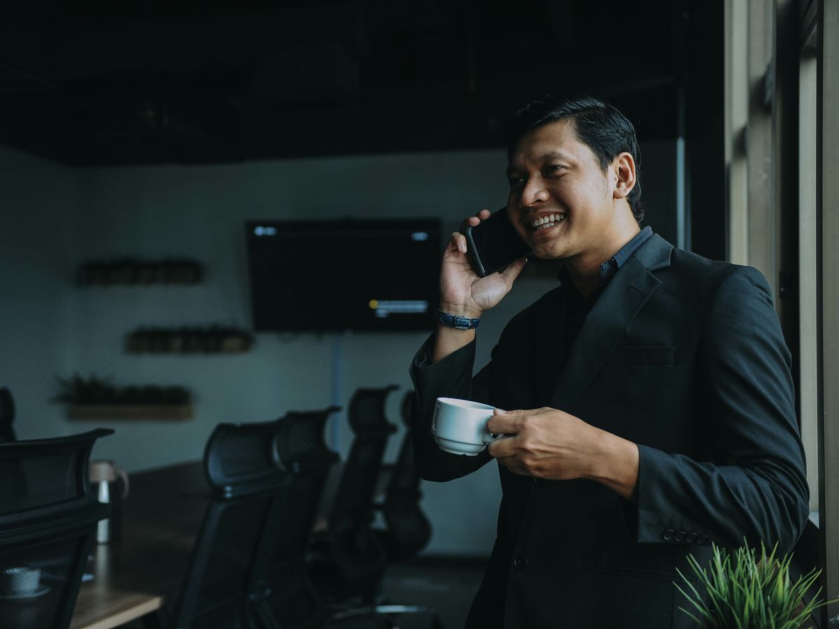 smiling man holding cup and using smartphone