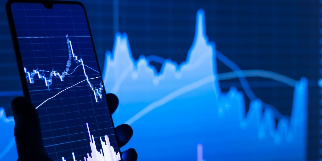 a person holding a cell phone in front of a stock chart