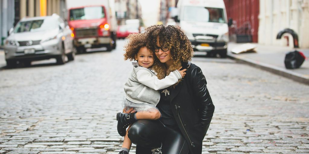 photography of woman carrying baby near street during daytime
