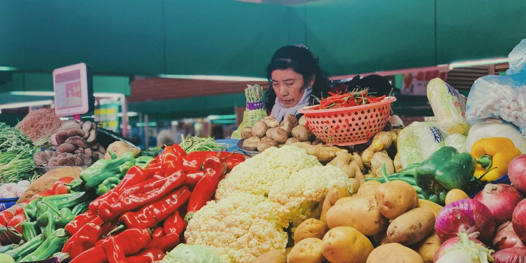 girl in red and white dress standing beside yellow and red fruit display