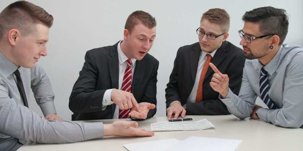 four men sitting at desk talking
