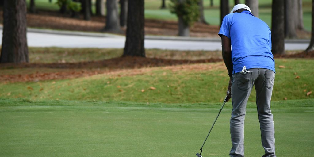 man in blue polo shirt and gray pants playing golf during daytime